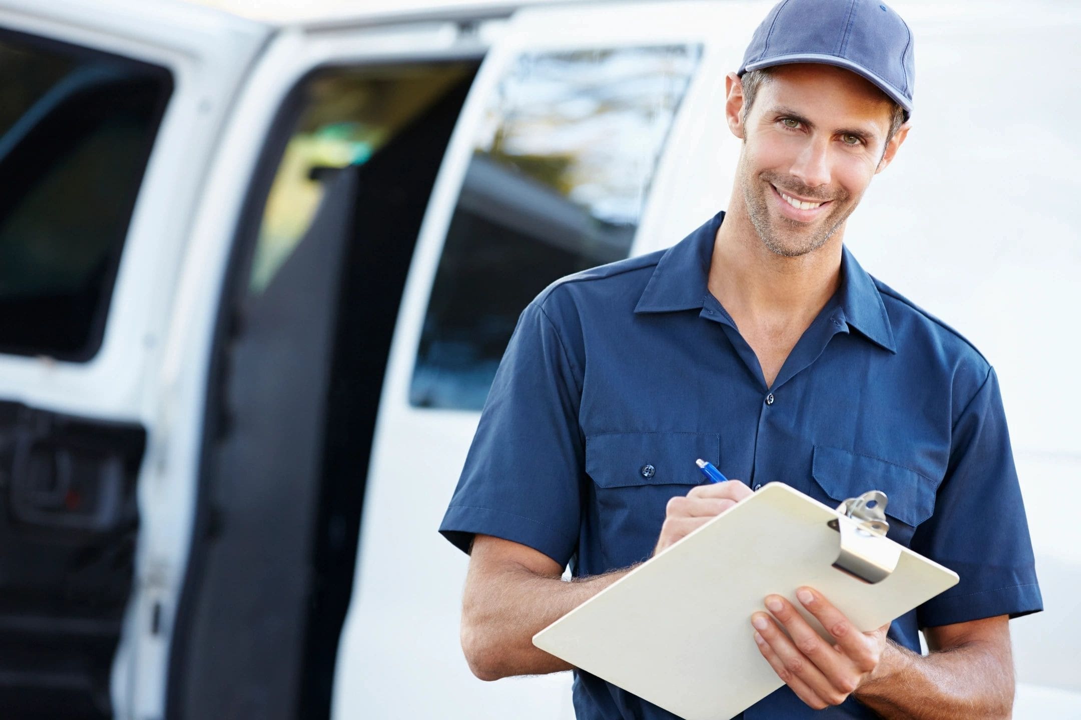 A man in blue shirt holding clipboard near white van.